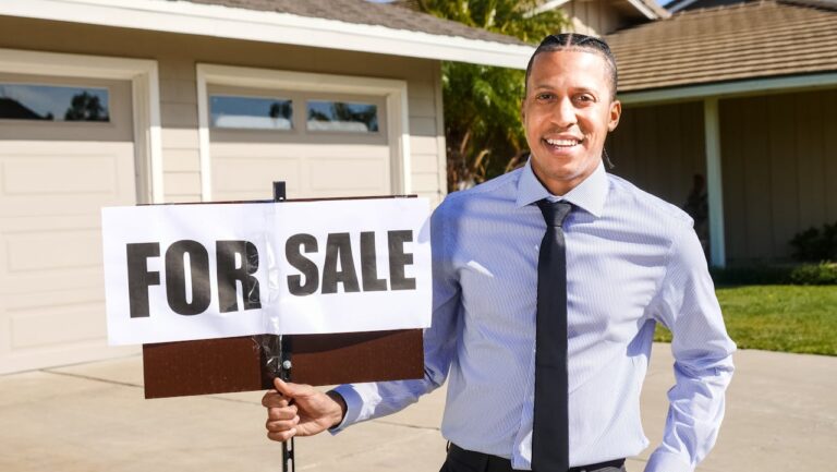 Smiling real estate agent with a for sale sign in front of a house