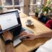 A person uses a laptop for internet browsing. A bright indoor setting with coffee on a wooden table.